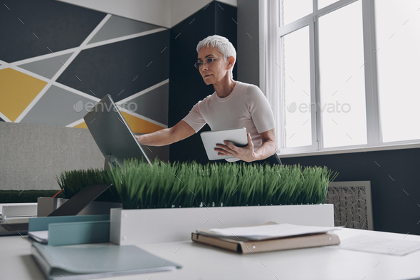 Concentrated senior businesswoman using technologies while working in office - Stock Photo - Images