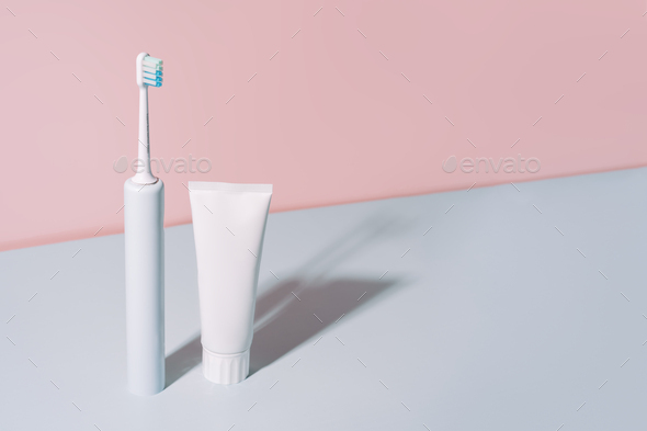 Electric toothbrush with toothpaste against a blue-pink background - Stock Photo - Images
