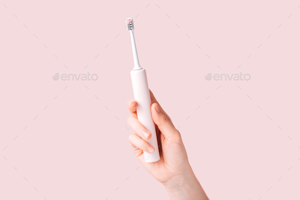 Electric toothbrush of pink color in female hand against pink background - Stock Photo - Images