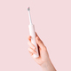 Electric toothbrush of pink color in female hand against pink background - PhotoDune Item for Sale