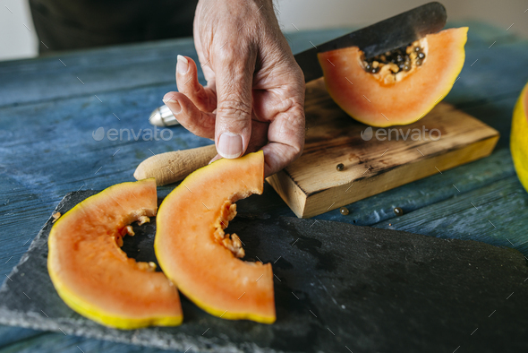 Close-up of man's hands placing pieces of papaya on slate plate