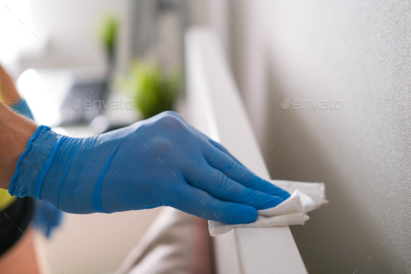 A man's hand in rubber gloves wipes the dust from the head of the bed with a napkin.