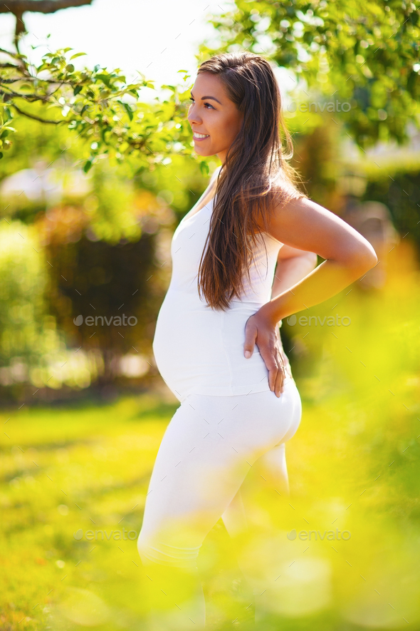 Pregnant woman in beautiful garden looking down at her belly - Stock Photo - Images