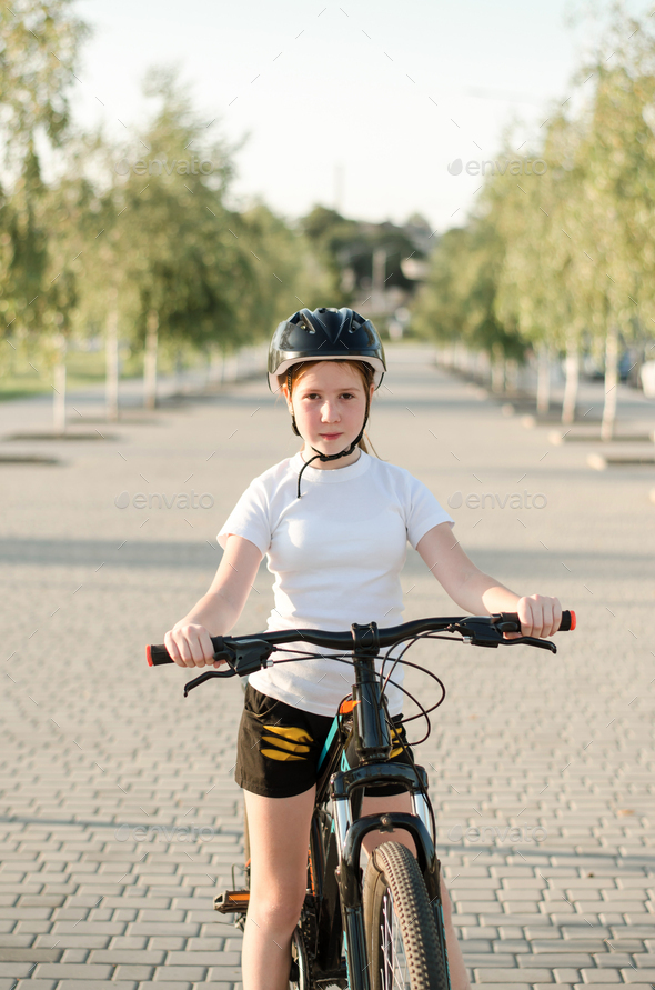 Girl 11 years old in the park with a bicycle. Children s sports and a healthy lifestyle. Stock Photo by oleksandrsh