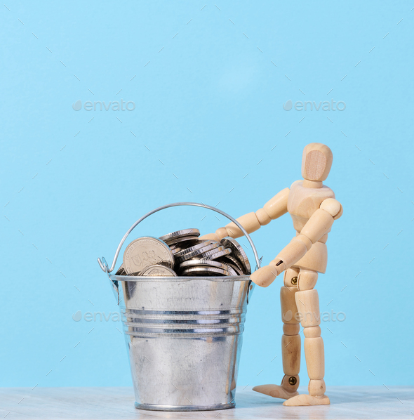 A wooden mannequin and coins in a miniature bucket on a blue background, a concept of high income
