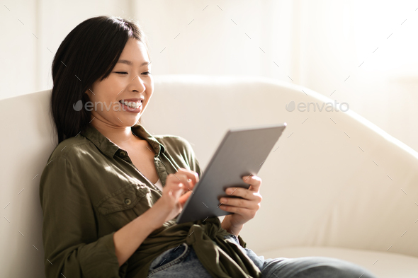 Relaxed asian woman reading blog on Internet, using digital tablet