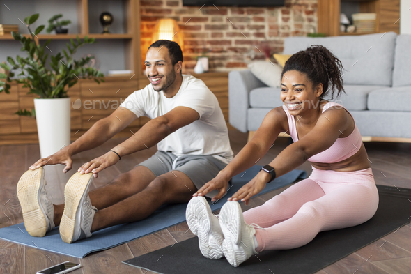 Glad young black couple in sportswear do leg stretching exercises