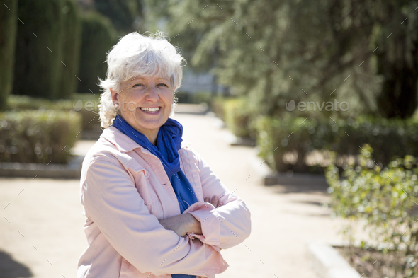 middle-aged woman with white hair smiling looking at camera with arms crossed in park - Stock Photo - Images