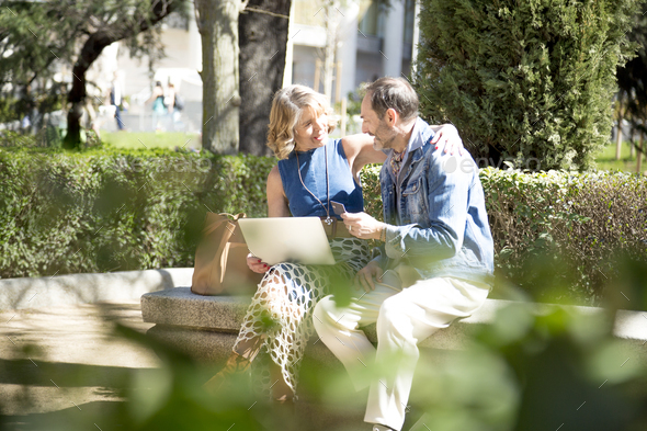 a middle-aged couple showing affection in the park while shopping online with their computer card - Stock Photo - Images