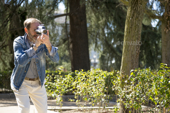 attractive middle-aged photographer taking pictures in the park with a vintage camera - Stock Photo - Images