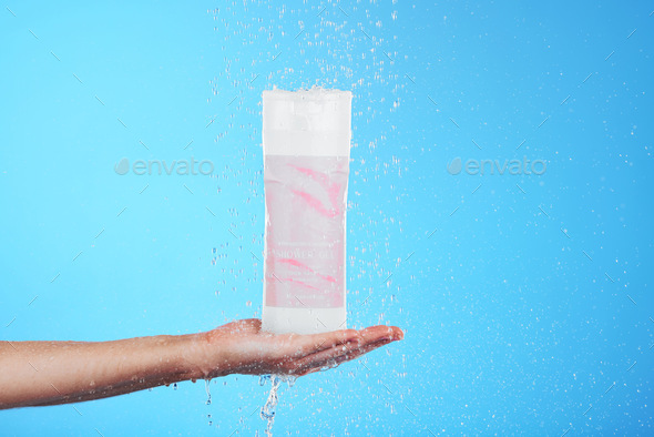 Shampoo, showing and hand with a bottle in the shower isolated on a blue background in studio. Clea - Stock Photo - Images
