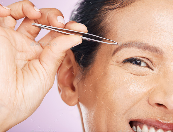 Woman with tweezers for plucking eyebrows in studio for mature facial hair removal routine. Self ca