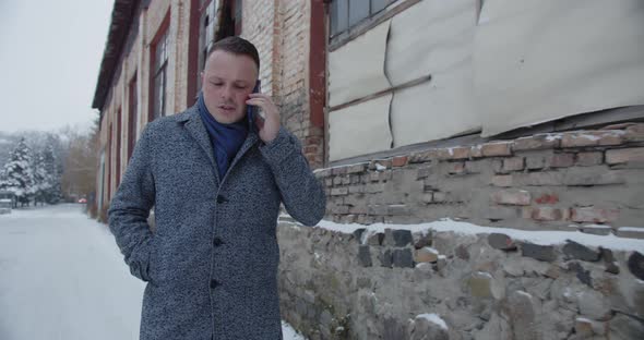 A Man Walks In A Snowy City Near An Old Building And Talks On A Mobile Phone