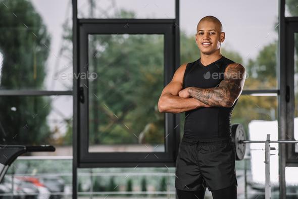 portrait of african american sportsman posing with crossed arms at gym - Stock Photo - Images