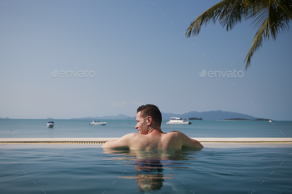 Rear view man while relaxing in swimming pool against sea - Stock Photo - Images