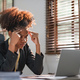 Young African American woman with afro hairstyle looks annoyed and stressed, sitting at the desk - PhotoDune Item for Sale