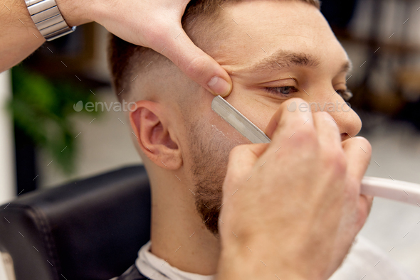 Barber shaving bearded man with retro knife