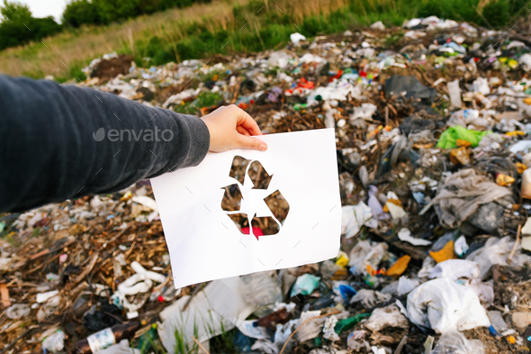 Garbage pollution. Hand holding cut paper with the logo of recycling on dump garbage trash backgroun