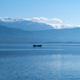 Greece Pamvotis Lake, Ioannina city Epirus. Boat on water, snowy mountain peak, blue sky background. - PhotoDune Item for Sale