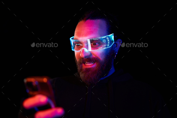 Dark portrait of a surprised man using a mobile and a extended reality reality goggles