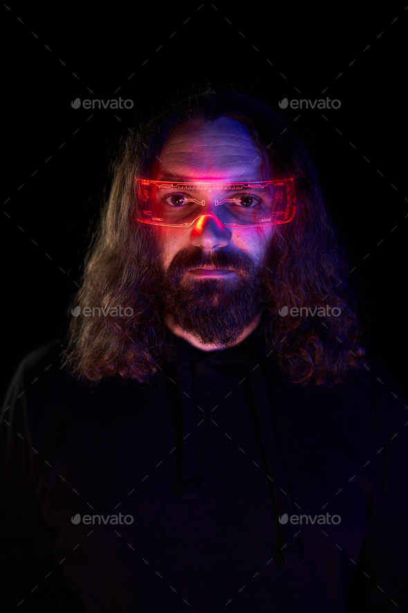 Vertical dark portrait of a man using extended reality goggles illuminated with red neon lights