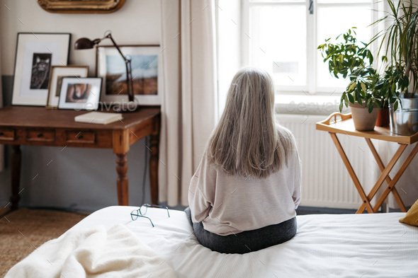Rear view of senior woman sitting on a bed. - Stock Photo - Images