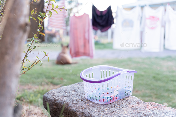 Close up of a clothespin basket in a garden surrounded by hanged up clothes in a rope