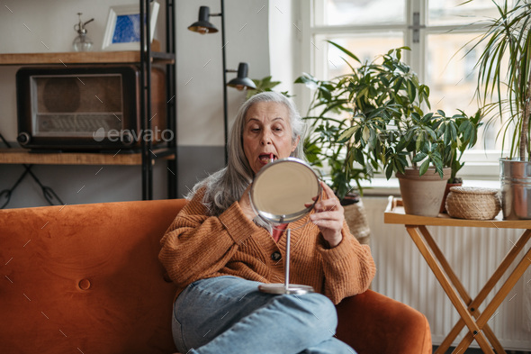 Senior woman doing her make-up, sitting in a living room. - Stock Photo - Images