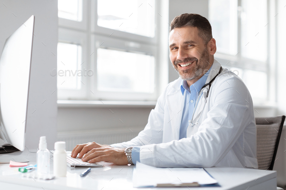 Happy male doctor medic expert using computer at work in hospital, checking patients electronic