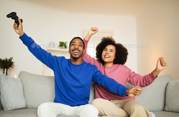 Happy Black Couple Winning Videogame Shaking Fists Sitting At Home