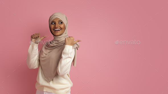 Cheerful muslim woman in hijab pointing at copy space behind her back