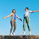 Two young girl dancing, having fun and fooling on big stone in seaside with blue sky background. - PhotoDune Item for Sale
