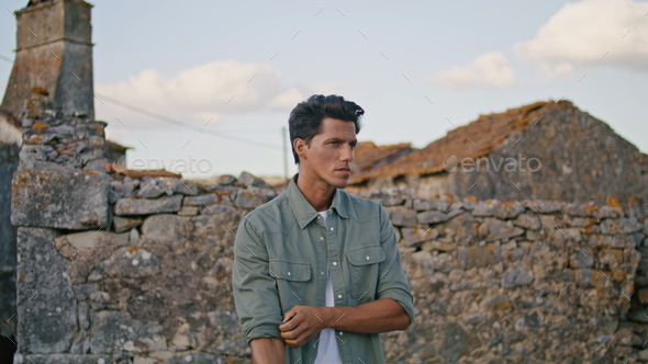 Serious man looking distance at stone wall closeup. Worker rolling up sleeves