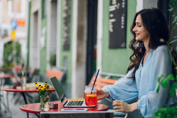Beautiful woman sitting in a street cafe and using laptop - Stock Photo - Images