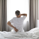 Unrecognizable grey-haired man sittting on bed, touching back and neck - PhotoDune Item for Sale