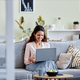 Woman using laptop sitting on sofa at home using internet or working online - PhotoDune Item for Sale