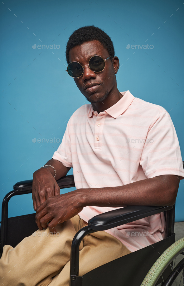 Fashionable black man with disability wearing sunglasses against blue background - Stock Photo - Images