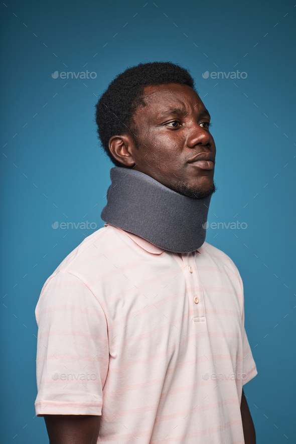 Black man wearing neck brace against blue background minimal - Stock Photo - Images