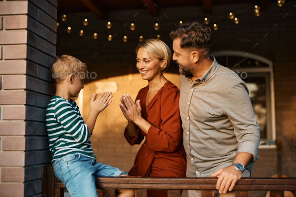 Happy kid playing clapping game with his parents on a patio.