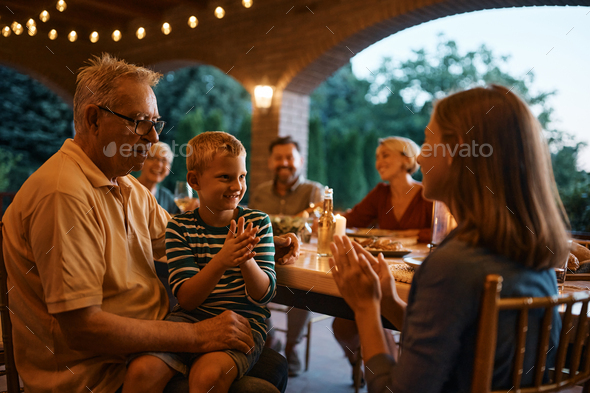 Happy kid and his sister playing clapping game during family dinner on a patio.