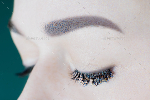 Close-up of closed eyes with artificial eyelashes, black eyeliner, ideal skin, eyebrows of