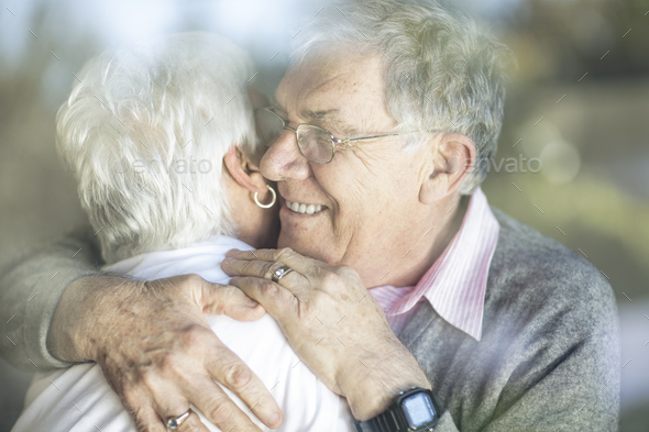 Happy senior couple hugging behind windowpane