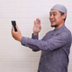 Asian muslim man using smartphone doing a video call and waving smile at phone - PhotoDune Item for Sale