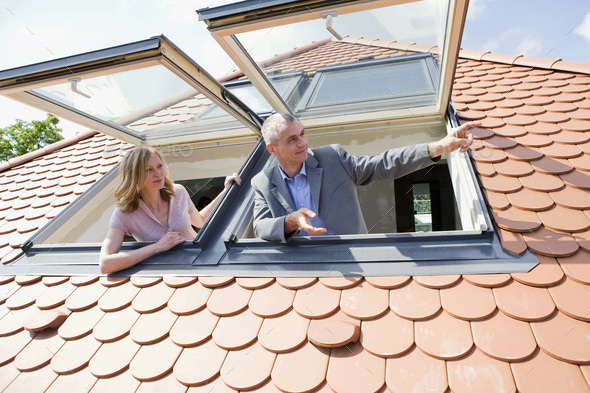 Couple looking out dormer windows, man pointing - Stock Photo - Images