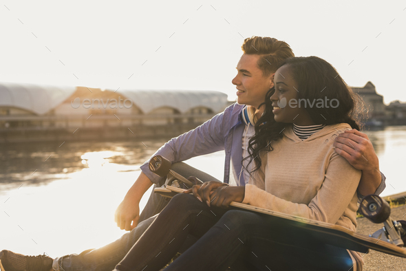 Young couple sitting at the river, watching sunset - Stock Photo - Images