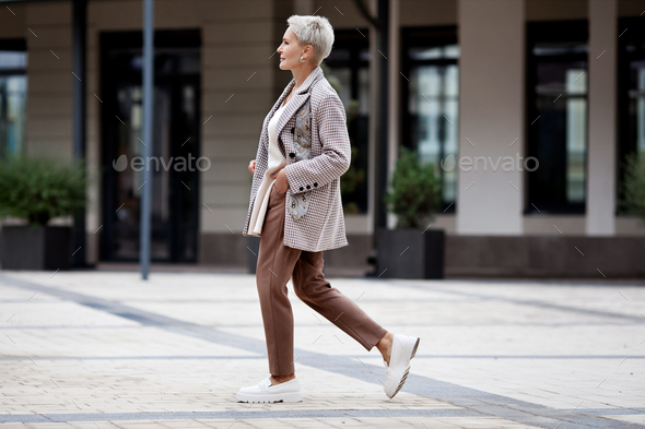 Side view full length woman walks outside and wear jacket, pants and loafer shoes