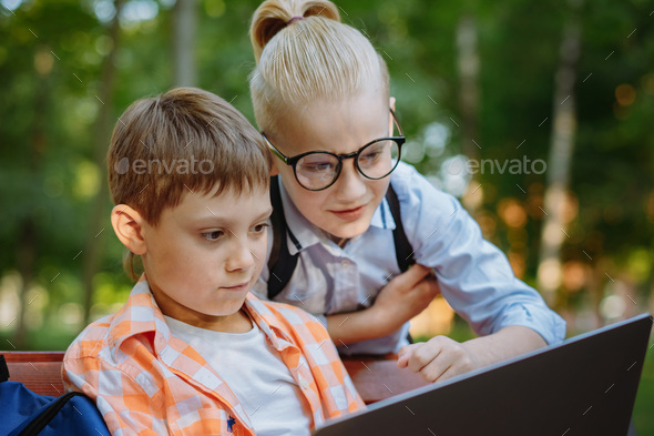 cute caucasian boys sitting on bench in park with laptop computer. Black screen - Stock Photo - Images
