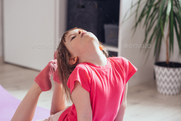 Child performs the exercise gymnastics at home on a mat
