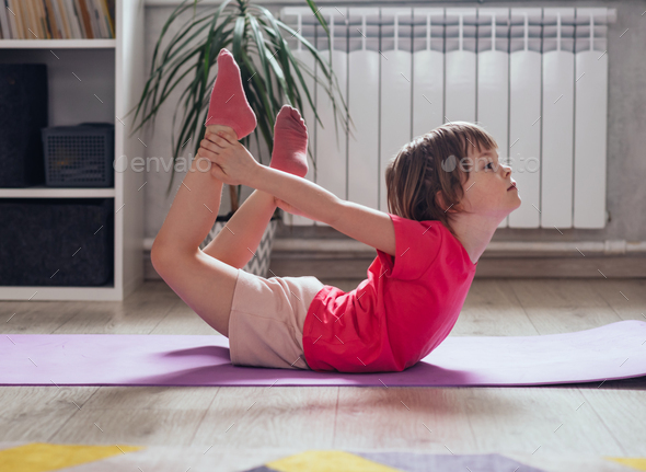 Child performs the exercise gymnastics at home on a mat