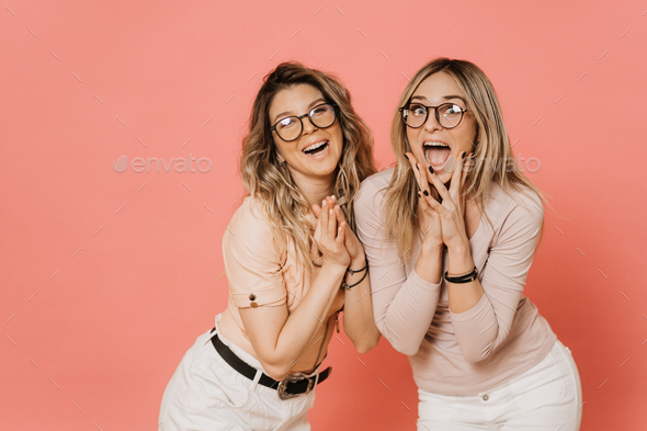Two pretty blondes in glasses in blouses and white jeans screaming and laughing with wide open mouth